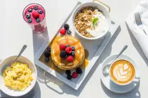 Brunch parisien vu de dessus : pancakes aux fruits rouges, oeufs brouillés, granola, cappuccino et smoothie