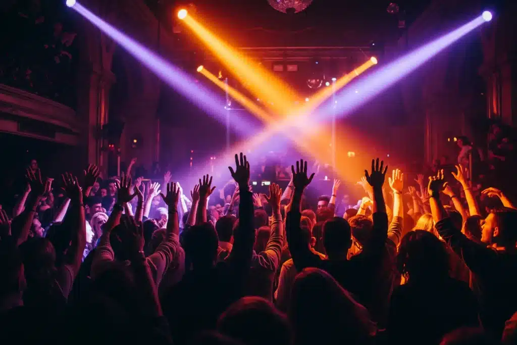 Boîte de nuit à Paris : foule qui danse bras levés sous des faisceaux violets et orangés sur une piste bondée