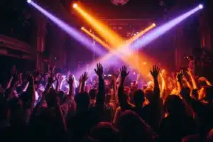 Boîte de nuit à Paris : foule qui danse bras levés sous des faisceaux violets et orangés sur une piste bondée
