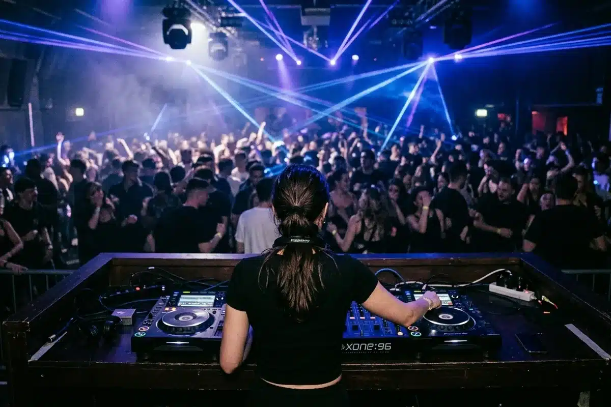 DJ de dos aux platines dans un club techno de Paris, faisceaux laser bleus au-dessus de la foule