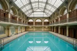Piscine parisienne de style Art déco, grand bassin turquoise sous une verrière, cabines en bois