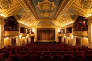 Intérieur d'une grande salle de cinéma Art Déco à Paris, rangées de fauteuils rouges et plafond décoré sous lumière dorée