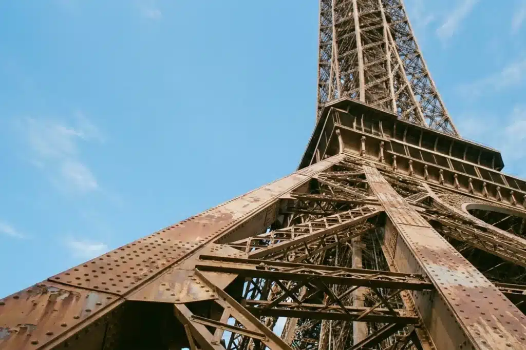 Contre-plongée sur la structure métallique de la Tour Eiffel avec le ciel bleu de Paris en arrière-plan