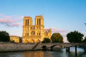 Vue extérieure de Notre-Dame de Paris depuis les berges de la Seine au lever du soleil, façade gothique dorée et pont en pierre